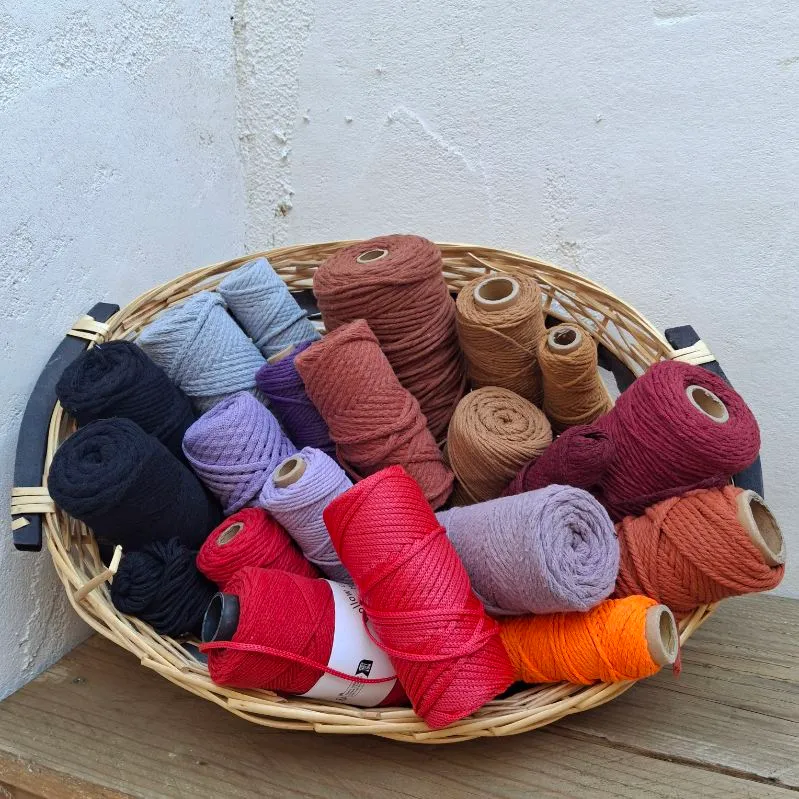 Panier en osier rempli de bobines de cordon de coton aux tons chauds : rouille, bordeaux, camel, rouge et lilas.