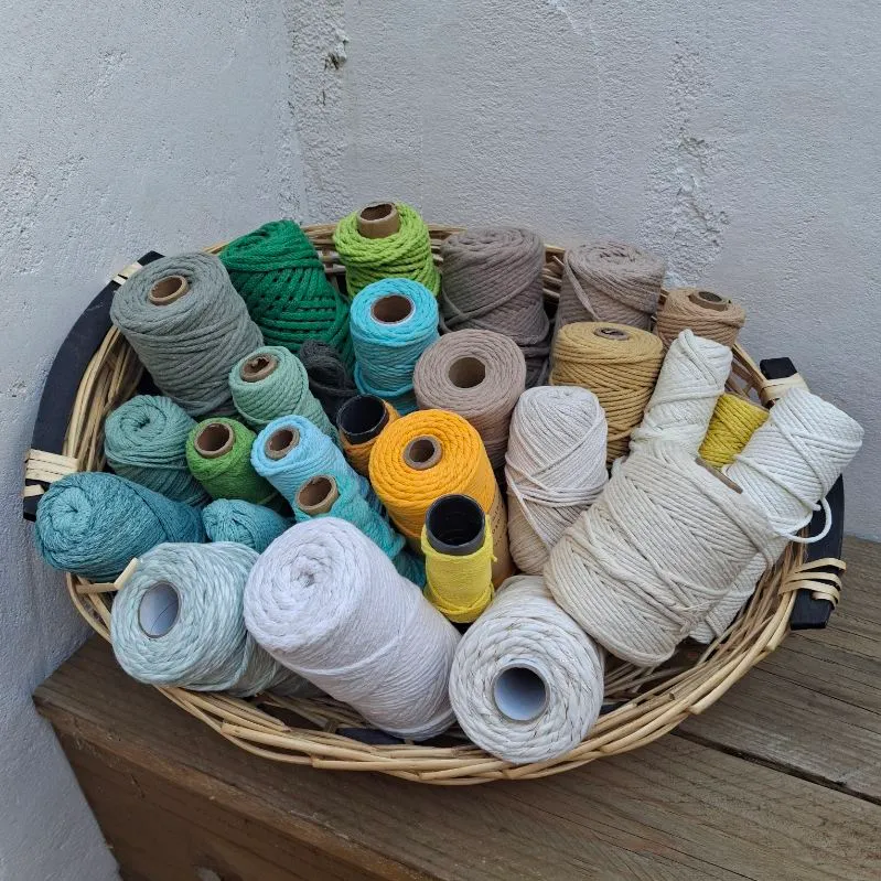 Panier en osier rempli de bobines de cordon de coton aux tons frais : sauge, turquoise, moutarde et écru.
